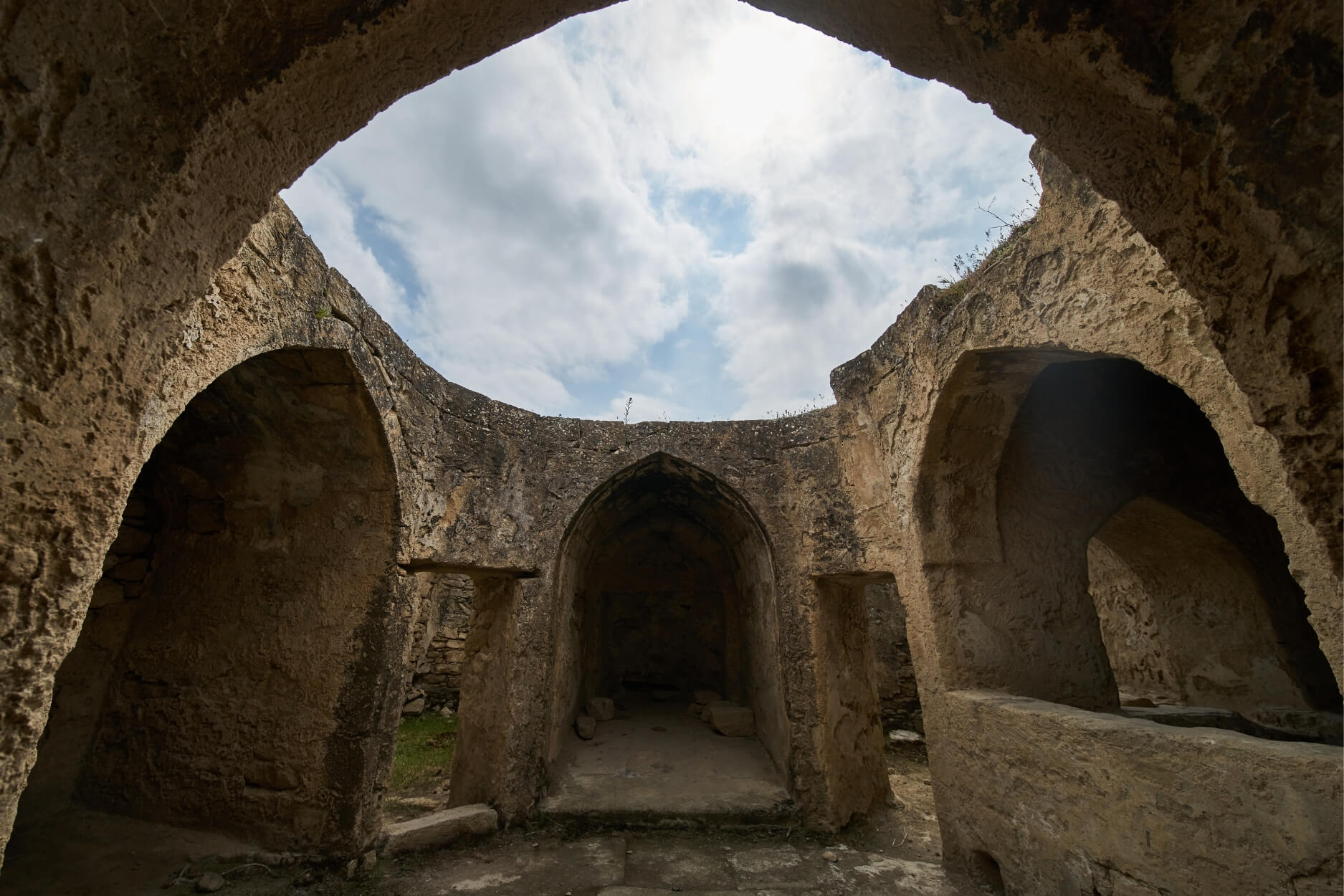 Stone ruins of an ancient bathhouse under an open sky, representing the timeless global practice of sweat rituals for purification and renewal.