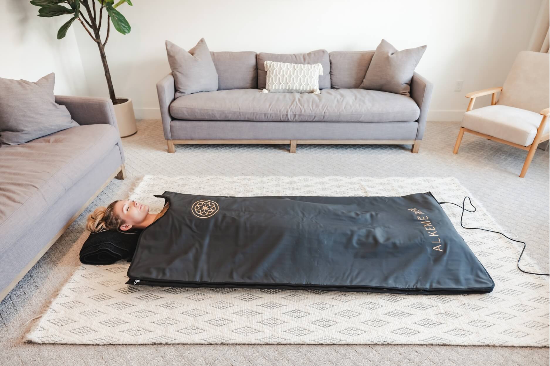 Woman resting inside an Alkēme Rise infrared sauna blanket in a peaceful home setting, representing modern wellness, warmth, and ritual.