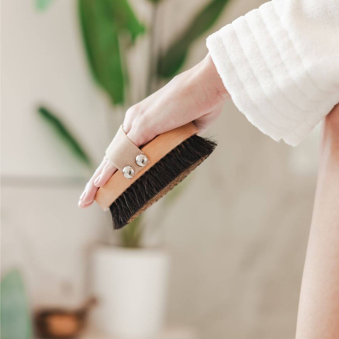 Hand brushing skin with the copper dry brush in a bright, serene bathroom before bathing.
