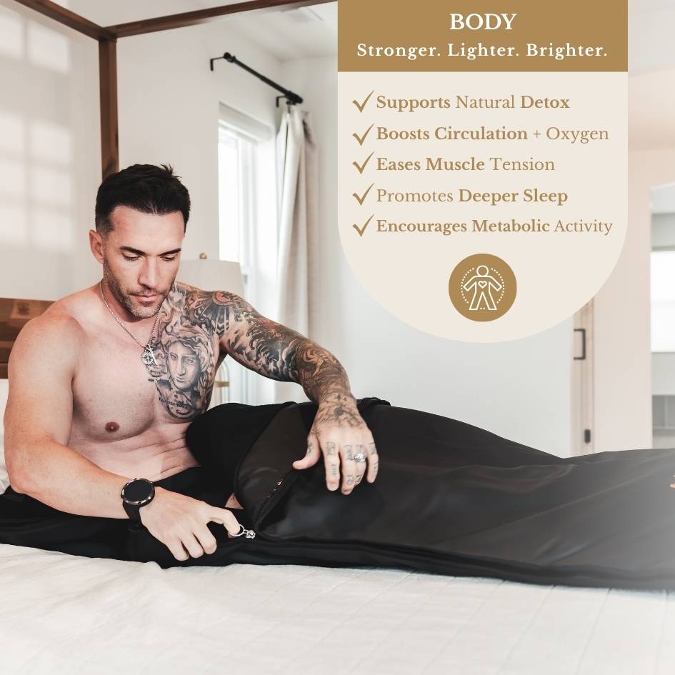 Man zipping into the black Alkemē Rise sauna blanket in a bed.