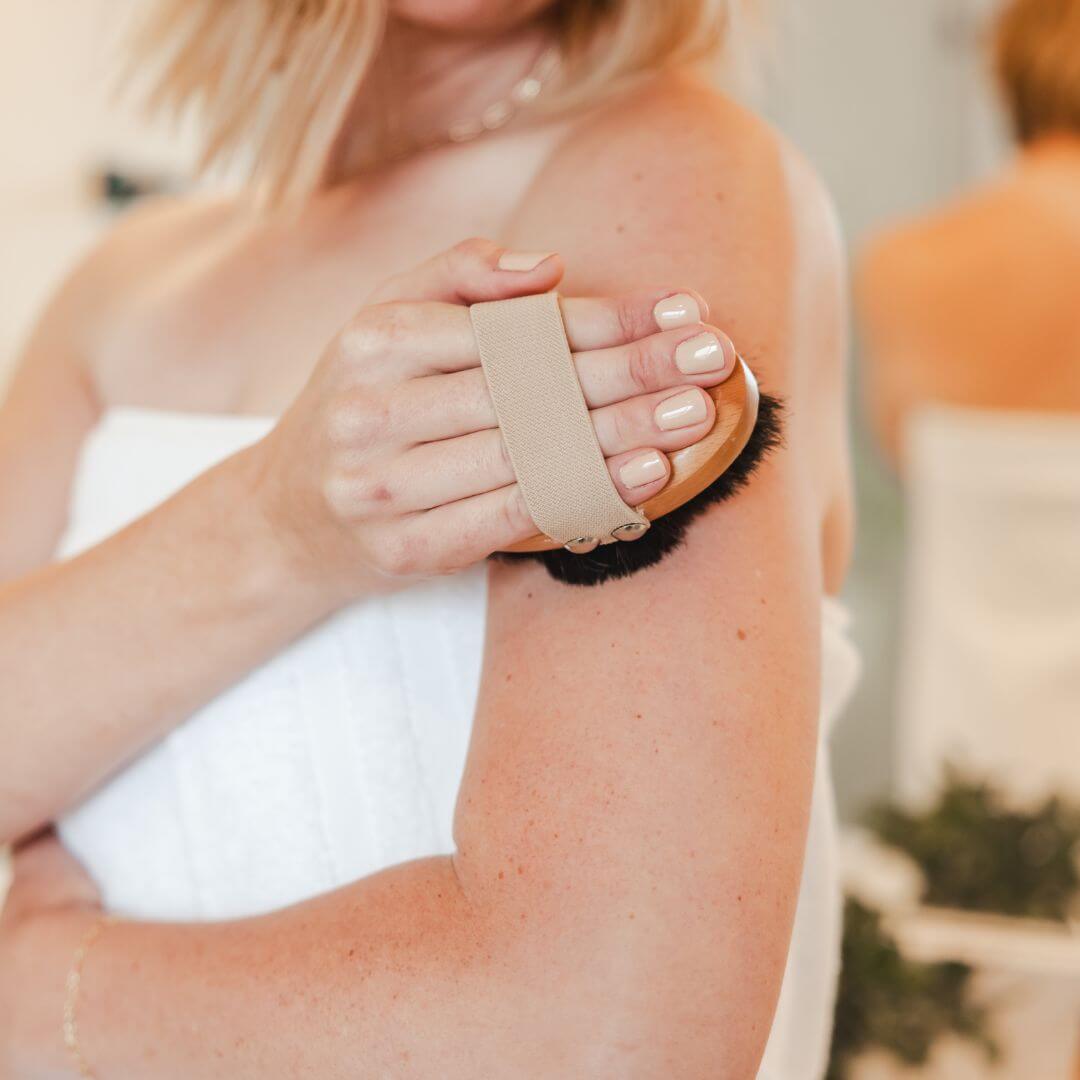 Focused image of dry brushing the shoulder with ion-charged copper bristles for a refreshing glow.
