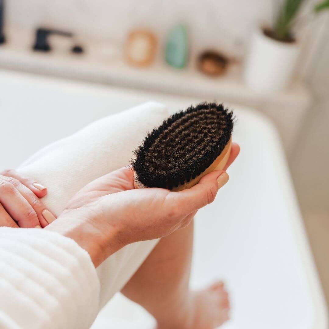 Close-up of the Alkemē Rise copper dry brush held in hand, highlighting the natural bristles and ergonomic shape.