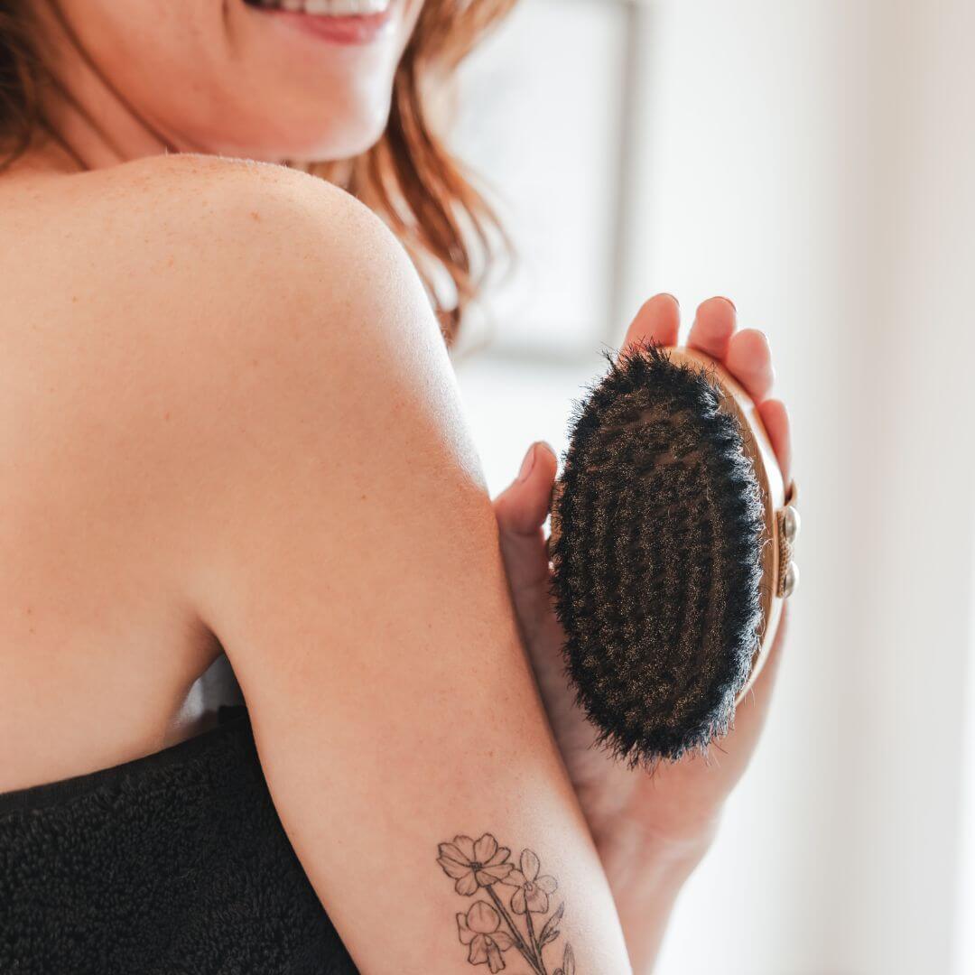 Hand brushing skin with the copper dry brush in a bright, serene bathroom before bathing.