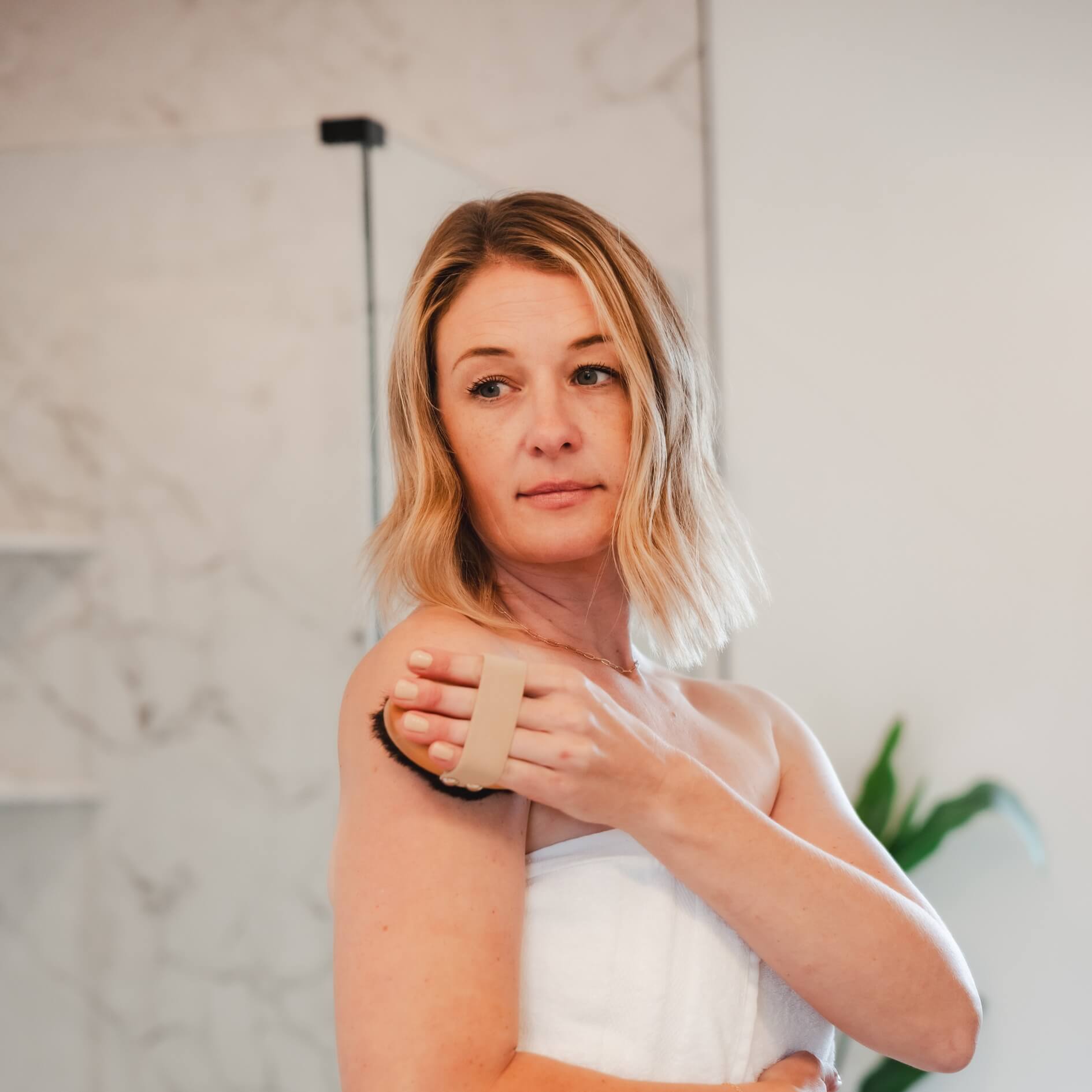 Woman using the Alkēme Rise copper dry brush on her arm, illustrating a glow-activating self-care ritual.