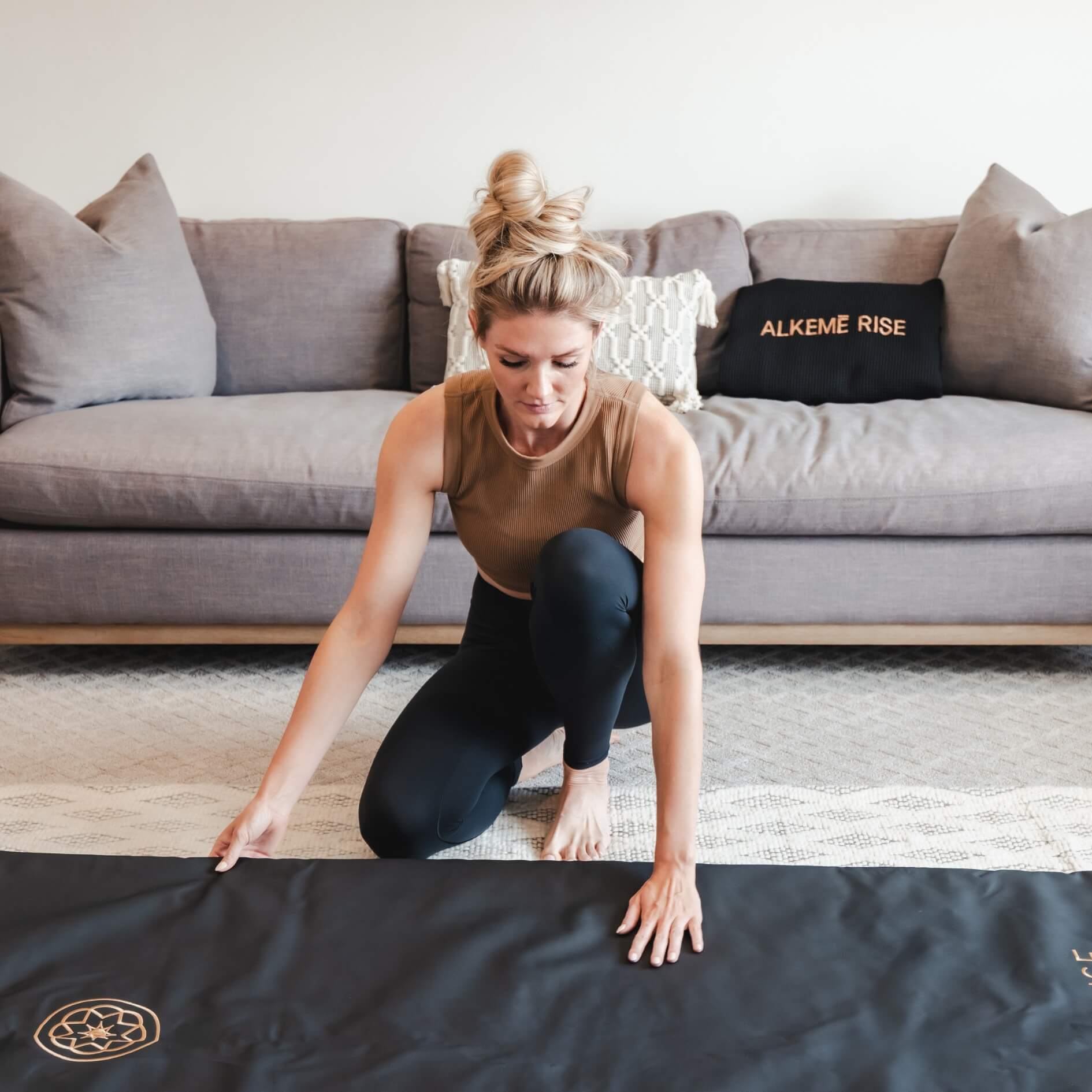 Woman kneeling on the floor setting up the Alkēme Rise black infrared sauna blanket, highlighting ease of use and elegant design.