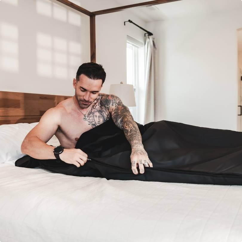 Man unzipping black Alkeme Rise sauna blanket to begin cool-down process after infrared session.