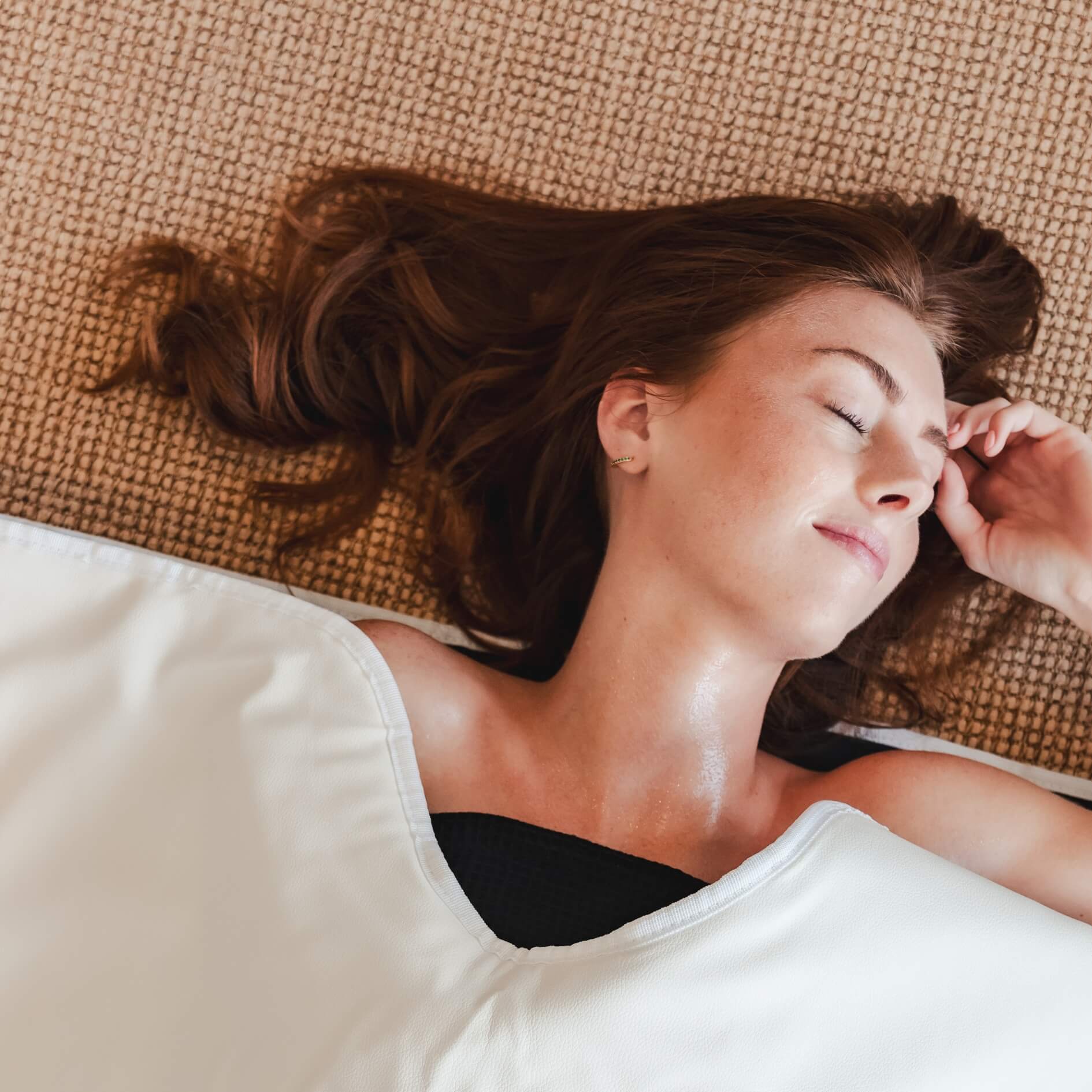 Woman lying peacefully inside the Alkēme Rise white infrared sauna blanket, showcasing at-home rejuvenation and deep relaxation.