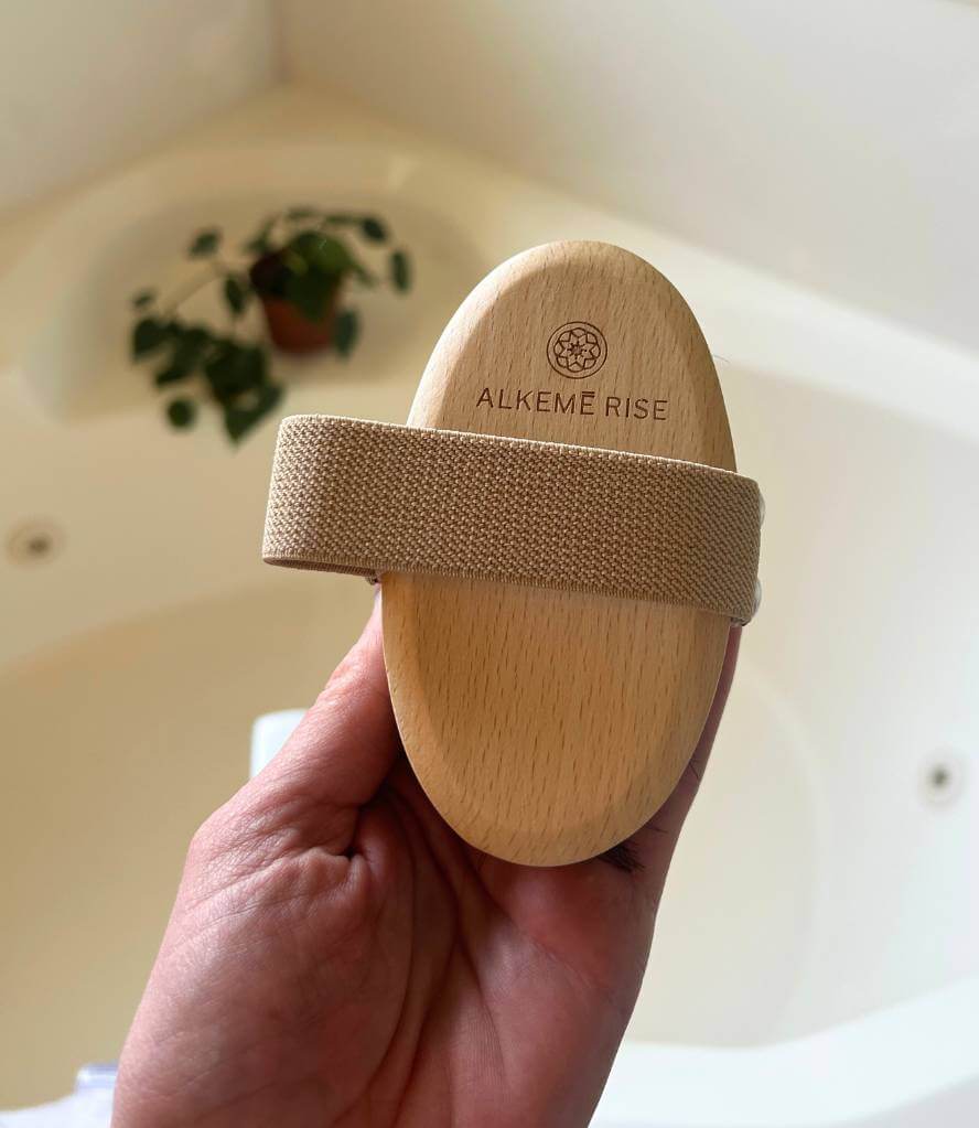 The Alkemē Rise Copper Dry Brush held in hand, displaying the engraved logo and natural wood handle for easy grip and beautiful craftsmanship.